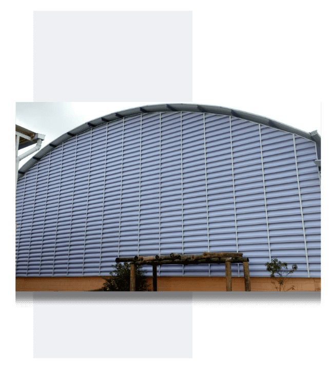 Venezianas Industriais para Fachadas A imagem da veneziana industrial Solution com aletas em PVC tem como finalidade apresentar de forma visual o produto em uso em um ginásio poliesportivo. As venezianas industriais Solution são ideais para quem busca uma solução em ventilação e iluminação natural para grandes espaços, como ginásios, lojas, fábricas e galpões.As aletas em PVC, por sua vez, conferem maior controle sobre a entrada de luz dentro do ambiente, permitindo regulá-la de acordo com a necessidade. Além disso, o PVC é um material leve, resistente e durável, ideal para projetos que exigem uniformidade, acabamento de qualidade e fácil manutenção. Dessa forma, a imagem da veneziana industrial Solution com aletas em PVC aplicada em um ginásio poliesportivo serve como uma representação clara e objetiva do produto em uso, evidenciando sua funcionalidade e eficiência em um ambiente real e destacando sua capacidade de melhorar o conforto térmico e luminoso do espaço.