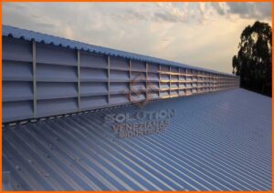 Lanternins e Seus Benefícios: Imagem mostrando lanternins instalados no telhado de uma estrutura, destacando seus benefícios. Os lanternins são visíveis como aberturas claras que permitem a passagem de luz natural e a ventilação eficiente. A ilustração enfatiza um ambiente iluminado e arejado, proporcionado por essas estruturas, destacando um espaço de trabalho ou residencial mais confortável e sustentável, com ênfase na saúde e bem-estar através da melhoria da qualidade do ar e redução do uso de energia.