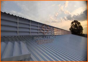 Lanternins E Seus Benefícios: Imagem ilustrativa mostrando um galpão industrial amplo e bem iluminado, equipado com lanternins no teto. Os lanternins proporcionam luz natural e ventilação eficiente, destacando-se contra o teto e permitindo a visão do céu claro. Dentro do galpão, trabalhadores realizam suas atividades em um ambiente arejado e confortável, ilustrando os benefícios dos lanternins em termos de economia de energia, melhoria da qualidade do ar e aumento do conforto térmico.
