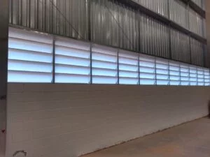 Imagem ilustrando a combinação de lanternins e venezianas em galpão industrial, promovendo ventilação natural e eficiência térmica.