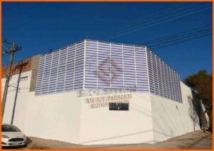 Veneziana Industrial e sua Eficiência A imagem mostra uma veneziana industrial elegantemente instalada em um galpão, permitindo a entrada de luz natural e a circulação de ar fresco. Visualmente, a veneziana combina perfeitamente com a arquitetura industrial, destacando-se como uma solução eficiente para ventilação e iluminação. No interior, pode-se observar um ambiente iluminado e arejado, onde os trabalhadores se beneficiam de condições de trabalho otimizadas. A fotografia captura o conceito de eficiência energética e conforto térmico proporcionado pelas venezianas industriais, enfatizando seu papel vital em promover um espaço de trabalho mais saudável e produtivo.